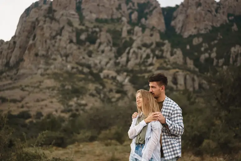Ein Paar steht in einer Umarmung vor einer Bergkulisse, symbolisiert Liebe und Sehnsucht nach einer Trennung.