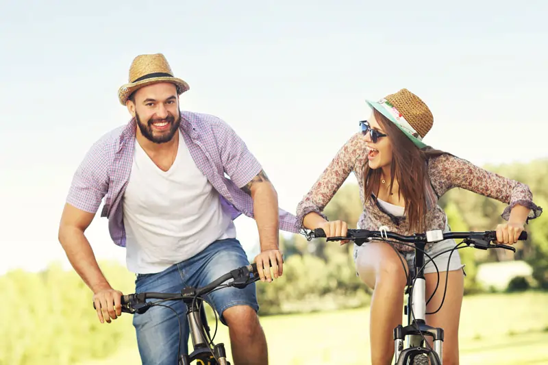 Ein glückliches Paar fährt gemeinsam Fahrrad in der Natur und lacht zusammen, um die Emotionen und die Freude an ihrer gemeinsamen Zeit auszudrücken.