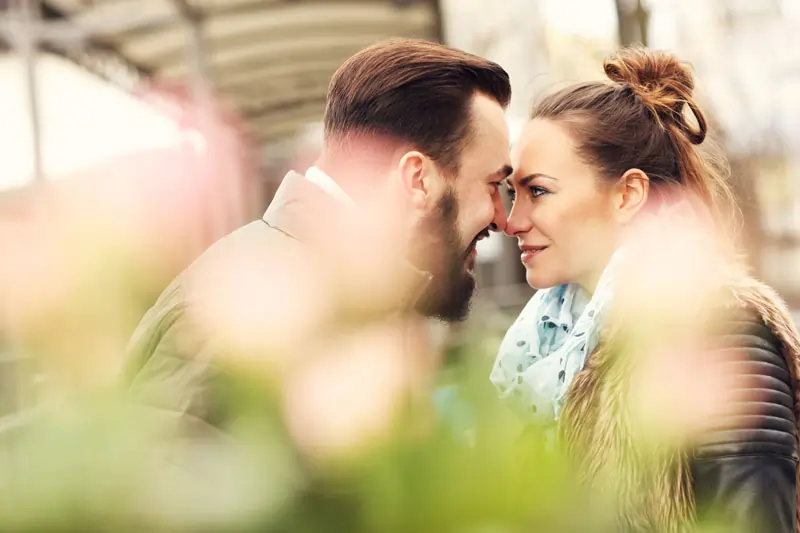 Ein Paar, das sich an einem romantischen Ort befindet und sich tief in die Augen schaut, mit Blumen im Vordergrund.