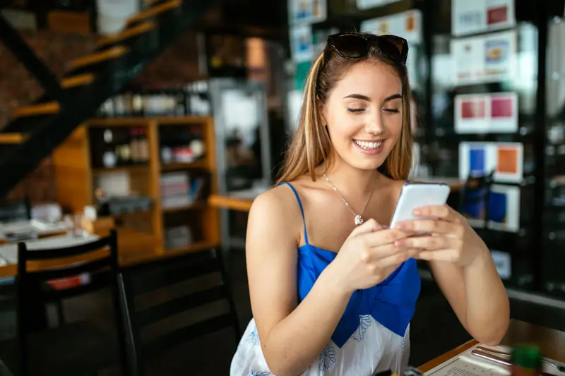Eine junge Frau lächelt, während sie eine romantische Nachricht auf ihrem Smartphone liest.