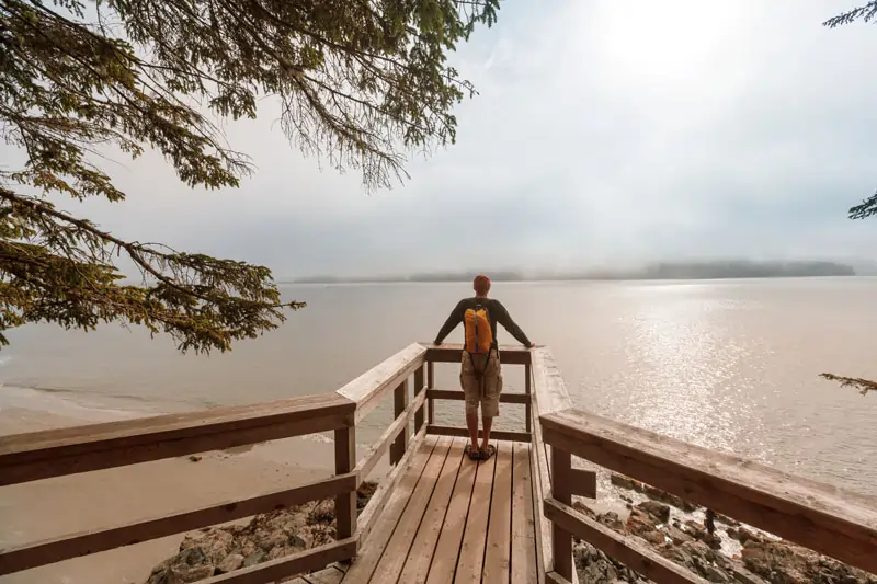 Ein Mann steht auf einem Holzsteg und blickt auf einen See, die Phasen des Entliebens reflektierend.