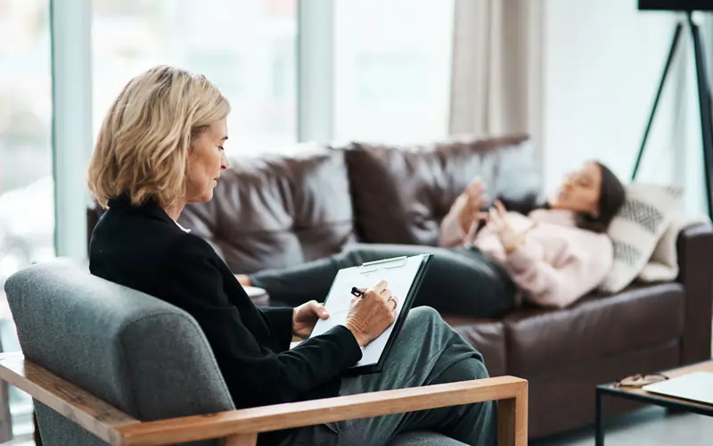 Reife Psychologin schreibt Notizen während einer Therapiesitzung, die sich mit dem Thema Entlieben beschäftigt.