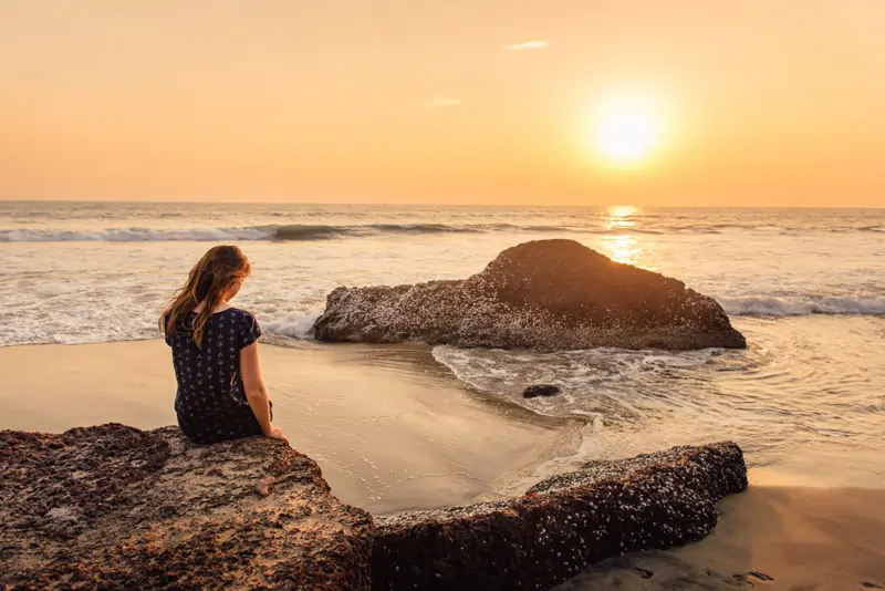 Frau sitzt nachdenklich am Strand bei Sonnenuntergang, nachdem er sich für eine andere entschieden hat.