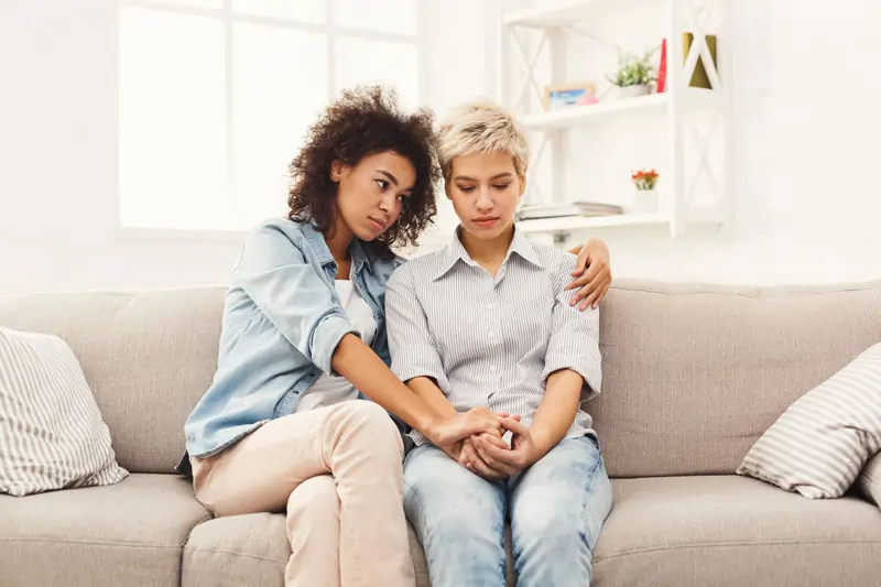 Zwei Frauen sitzen auf einem Sofa und sprechen über Probleme, um den Schock zu verarbeiten, dass er plötzlich eine andere hat.