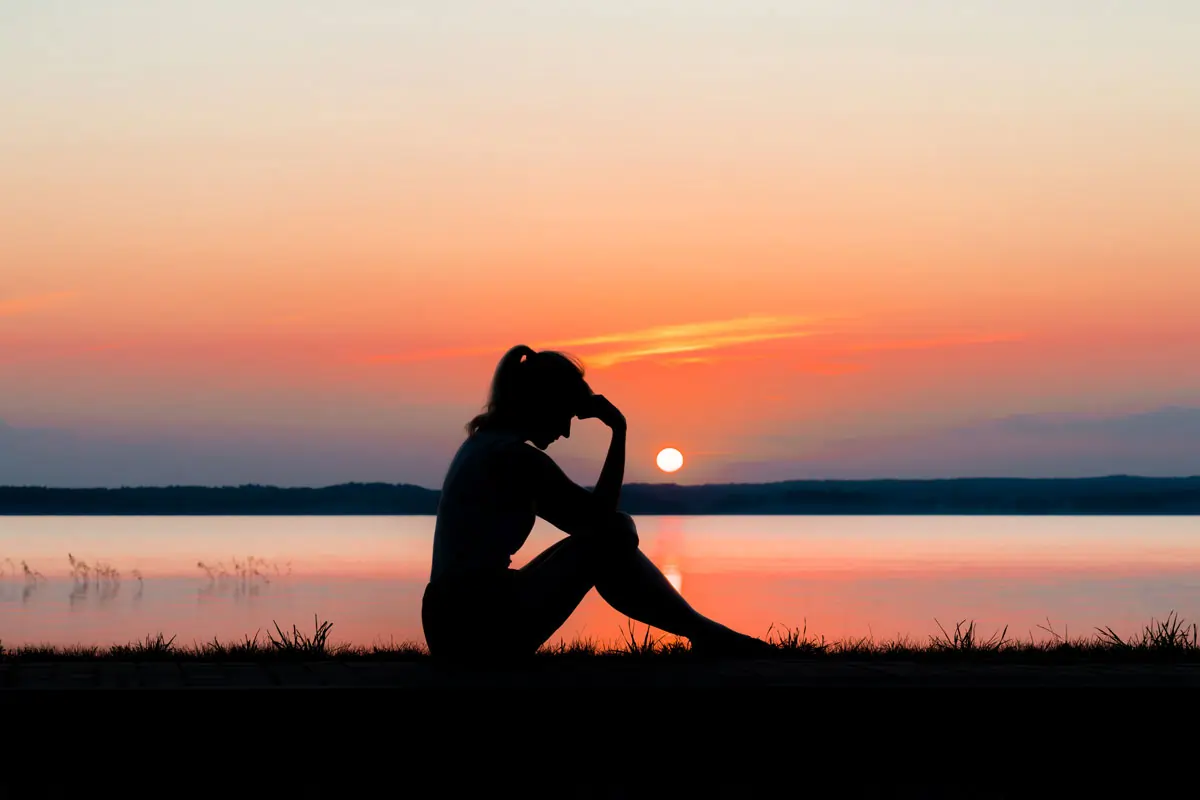 Nachdenkliche Frau am See bei Sonnenuntergang, die über die Frage "Wann vermisst er mich?" nachdenkt.